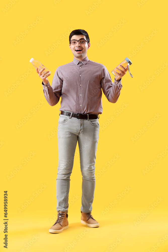 Young man with bottles of water on yellow background