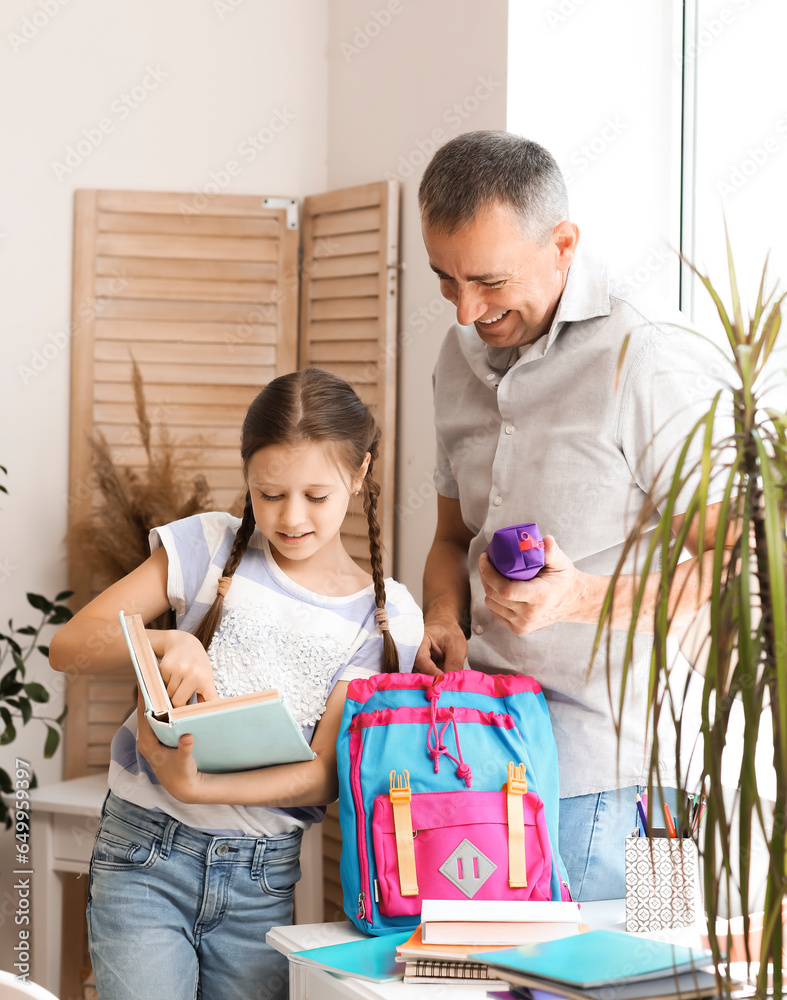 Father helping his little daughter to pack schoolbag at home