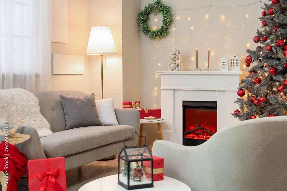 Interior of festive living room with fireplace, grey sofa and Christmas tree