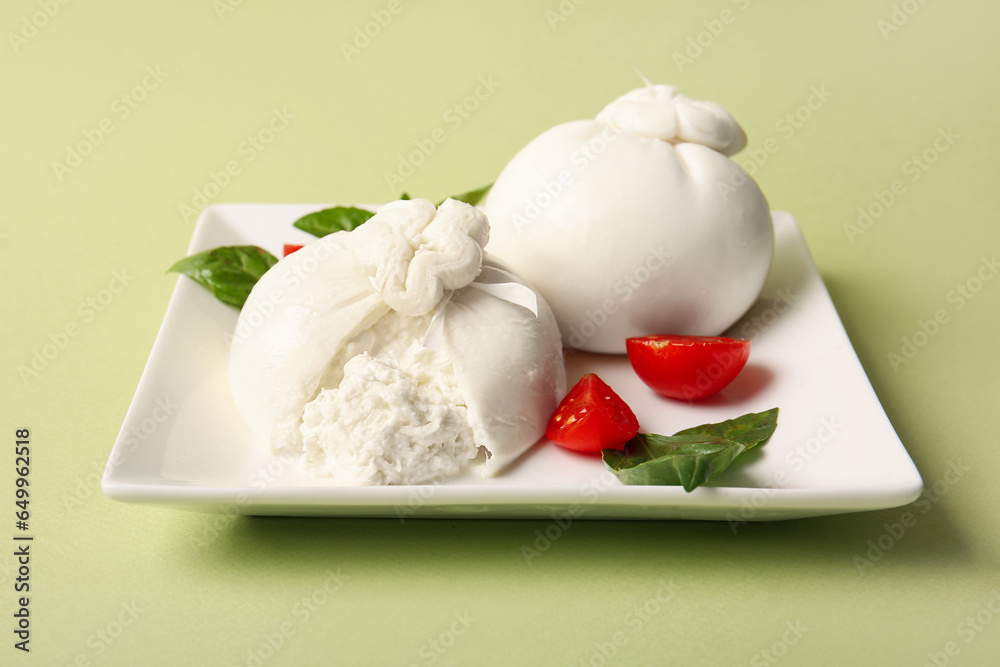 Plate with tasty Burrata cheese on green background