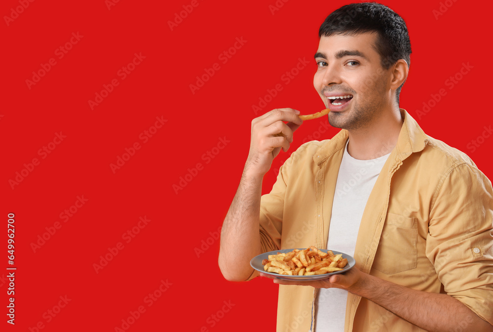 Young man eating french fries on red background