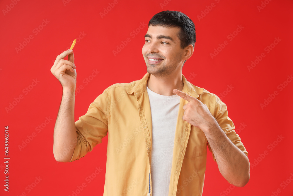 Young man pointing at french fries on red background