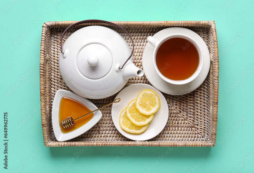 Wicker tray with teapot, cup of tea, honey and lemon slices on color background