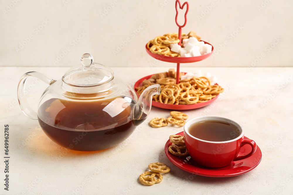 Teapot, cup of tea and pretzels on light background