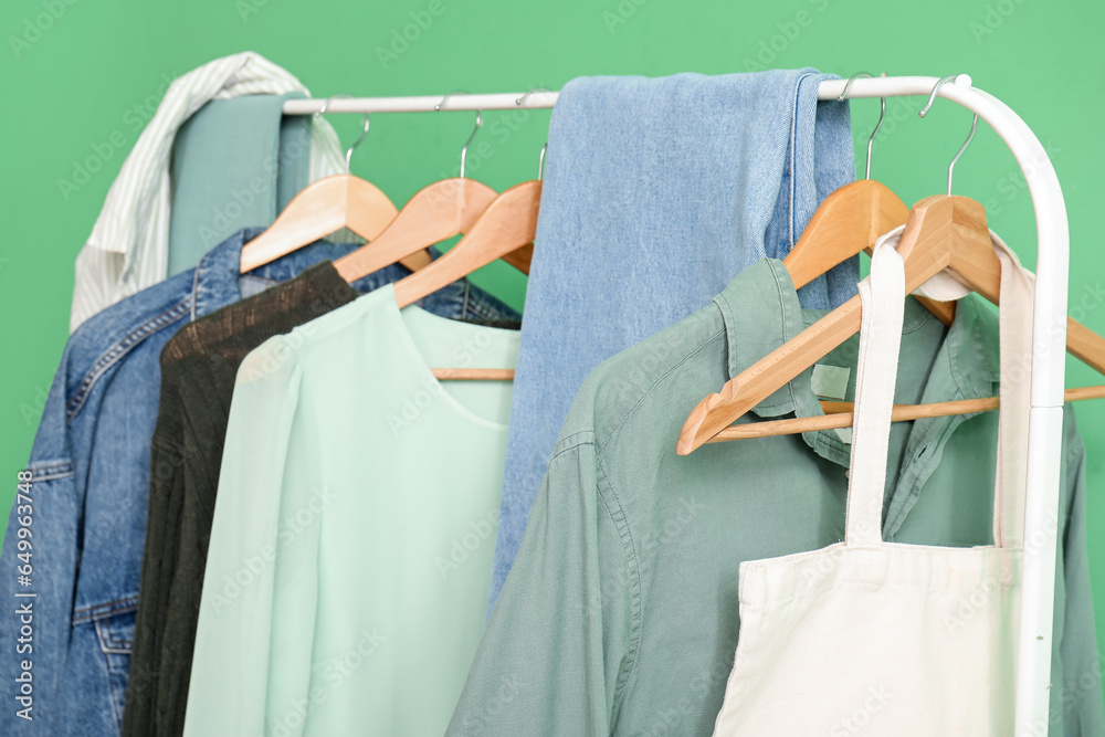 Stylish clothes and bag hanging on rack against green wall, closeup