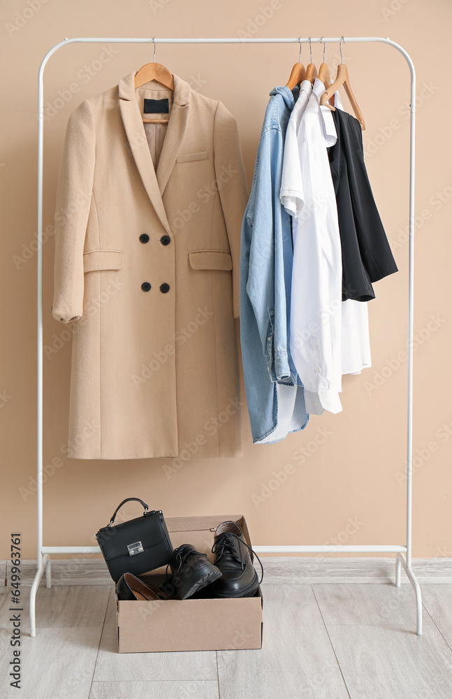 Rack with stylish clothes, bag and shoes against color wall