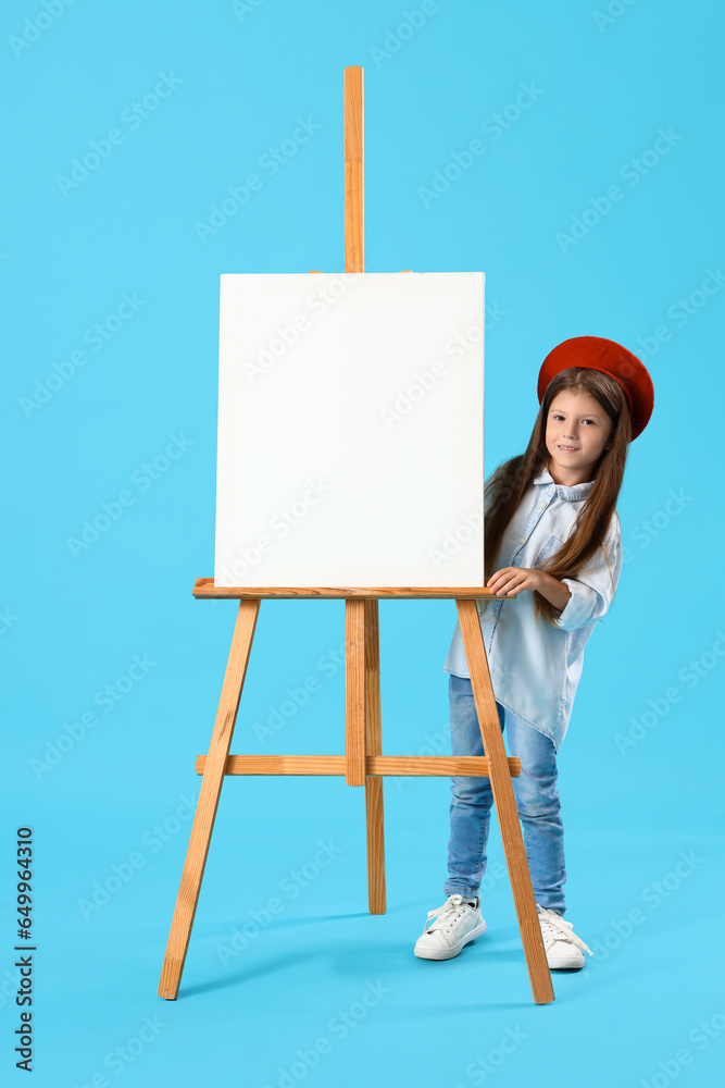 Cute little girl with easel on blue background