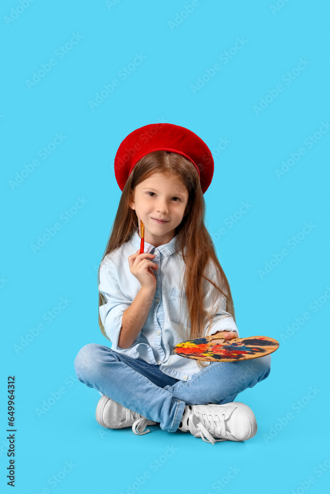 Cute little girl with paint palette and brush on blue background