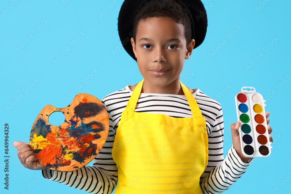 Little African-American boy with paints and palette on blue background