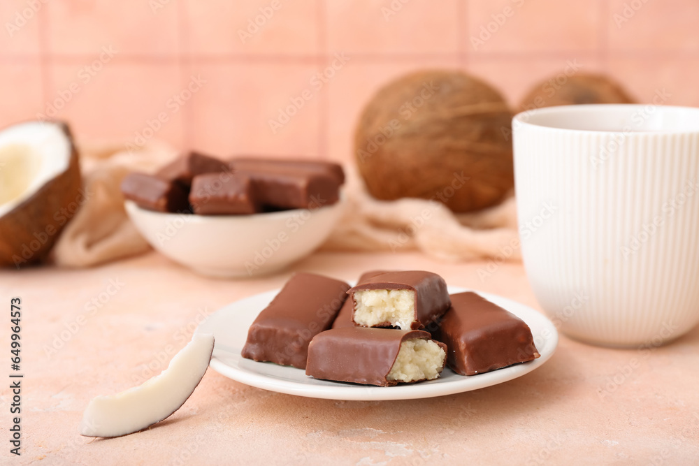 Plate with tasty chocolate covered coconut candies and cup of tea on table