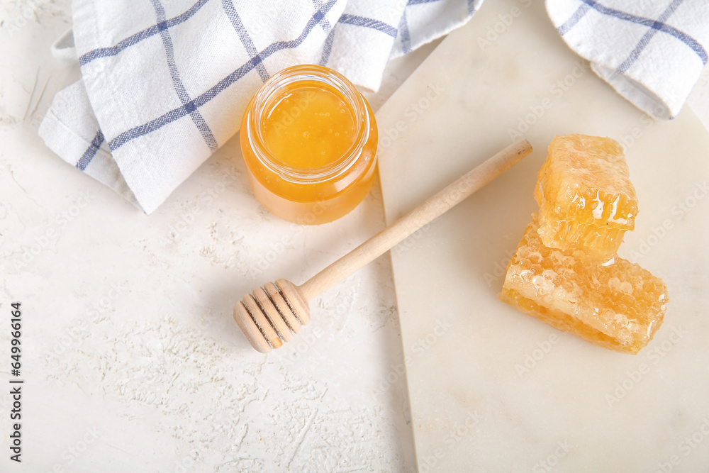 Jar of fresh honey, dipper and combs on light background