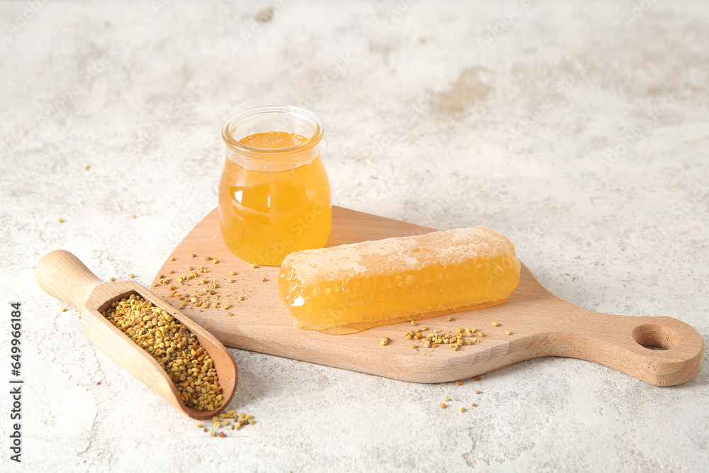 Wooden board with jar of honey, comb and bee pollen on light background