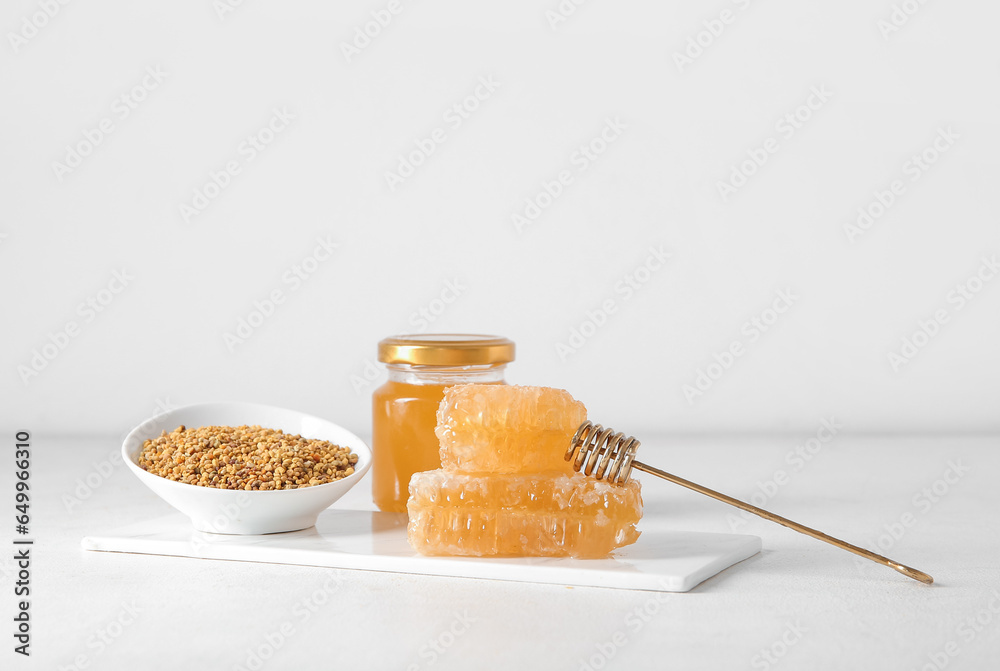 Board with bowl of bee pollen, honey and combs on light background