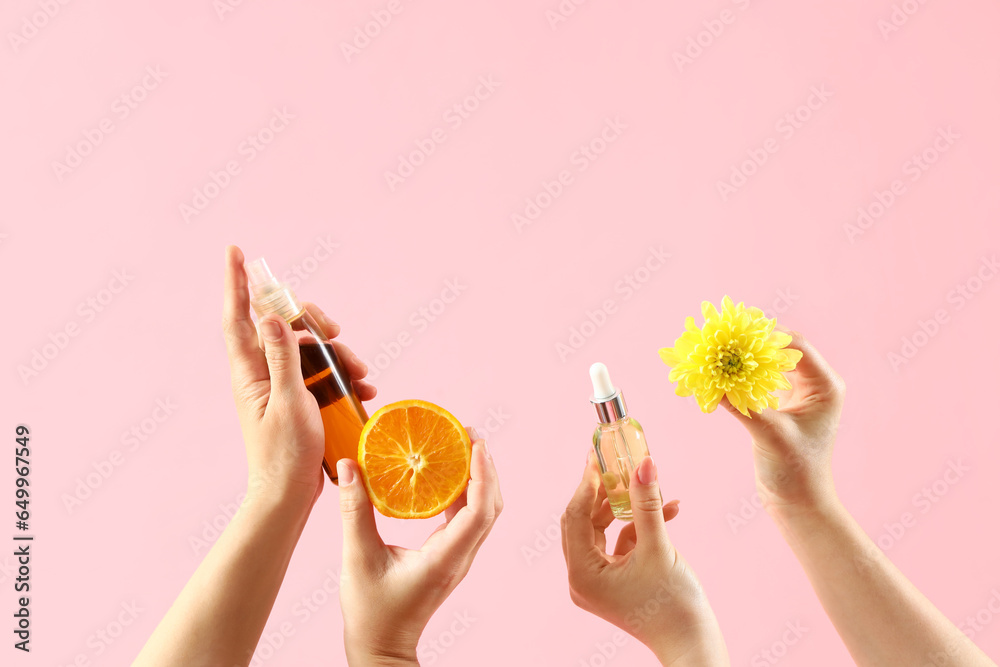 Female hands with cosmetic products, orange and chrysanthemum flower on pink background