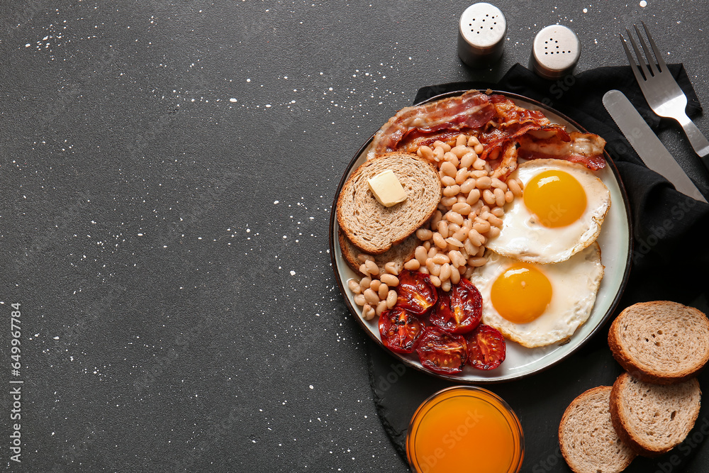 Plate with tasty English breakfast and glass of juice on black background