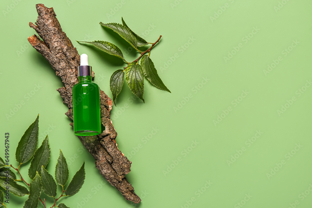 Bottle of cosmetic oil with tree bark and leaves on green background