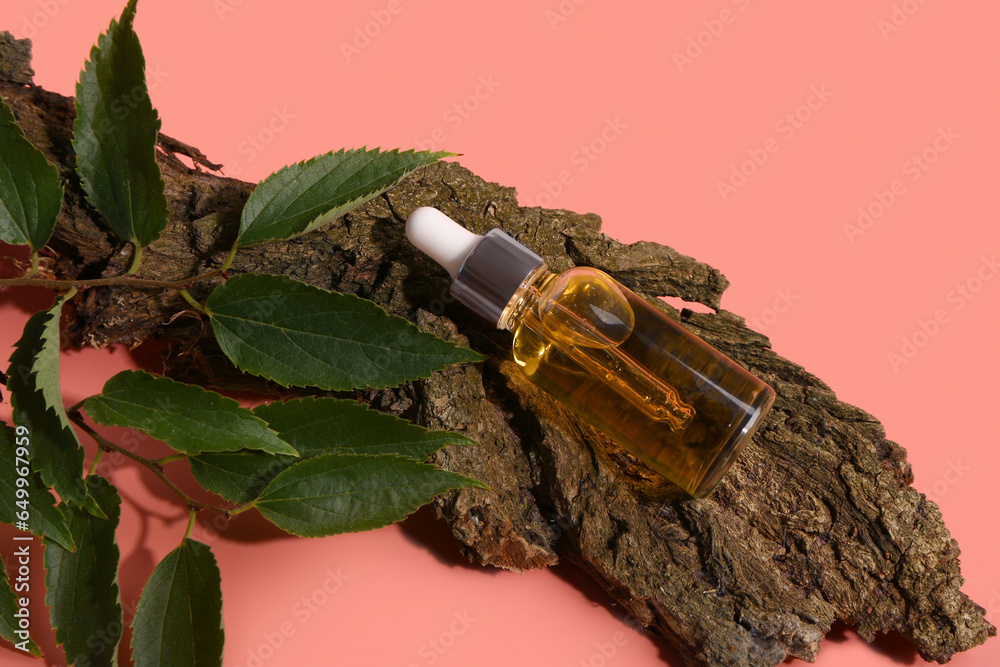 Bottle of cosmetic oil with tree bark and leaves on red background