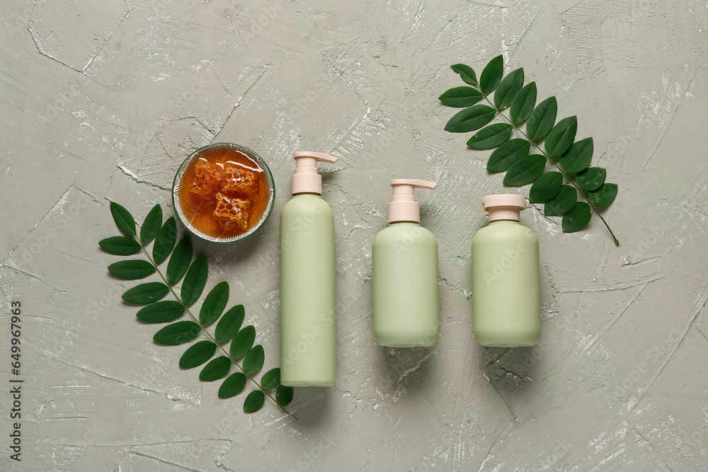 Bottles of cosmetic products with honey and leaves on light green background