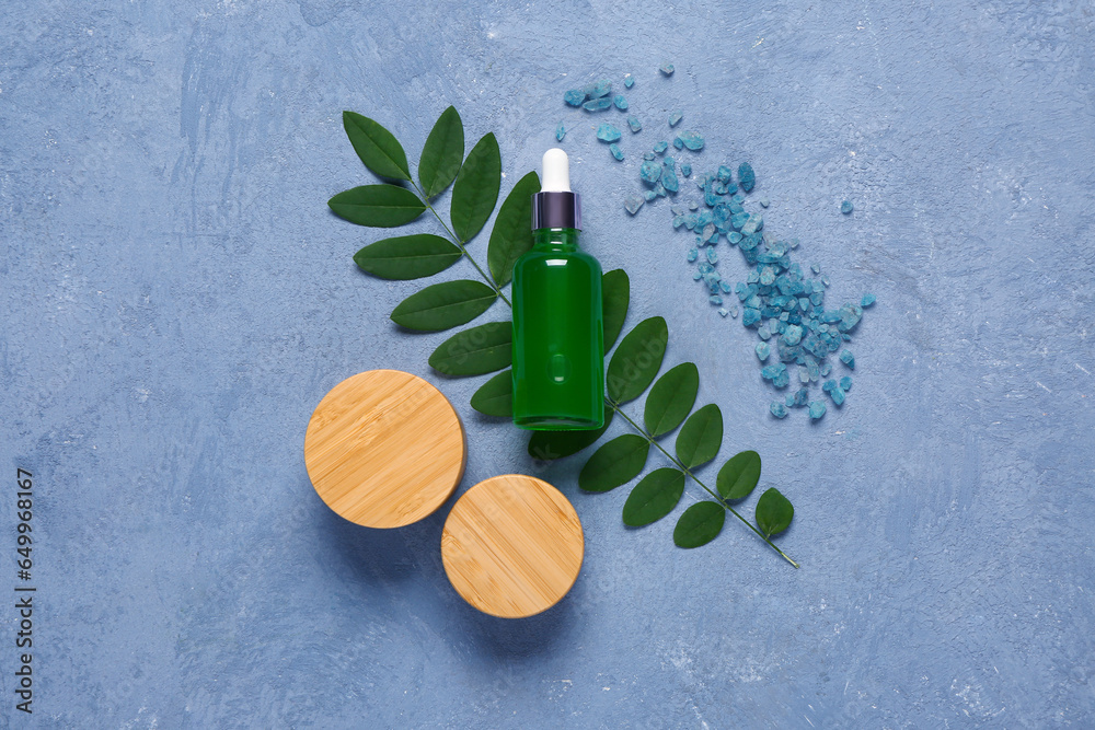 Bottle and jars of cosmetic products with sea salt on blue background