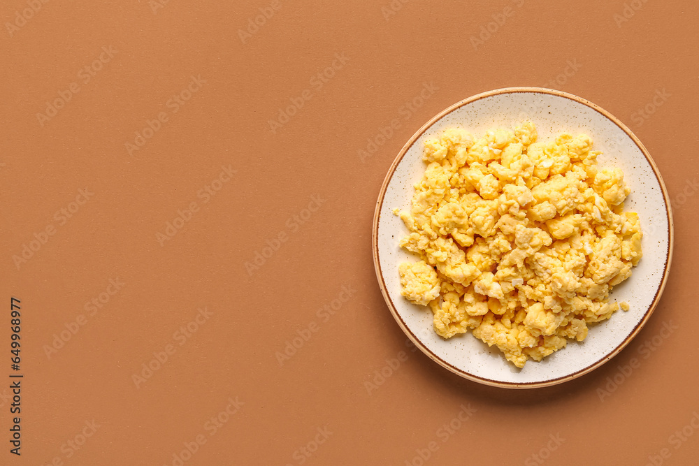 Plate of tasty scrambled eggs on brown background