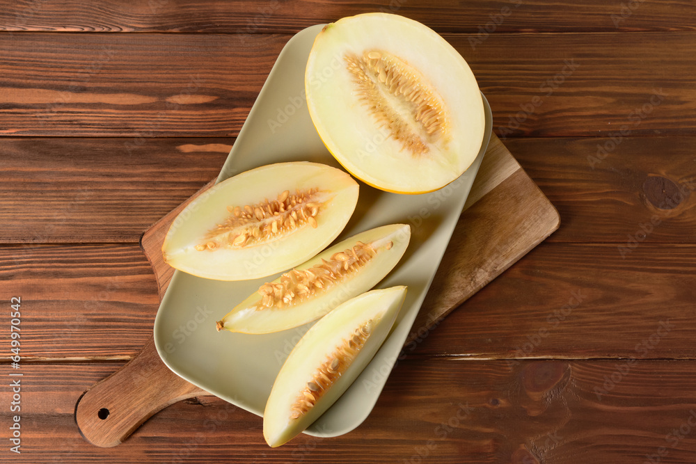 Plate with pieces of sweet melon on wooden background