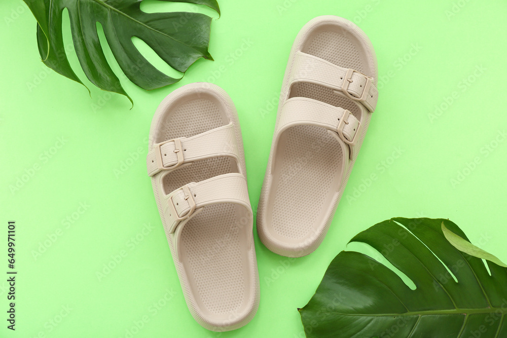 Pair of beige flip flops and tropical leaves on green background