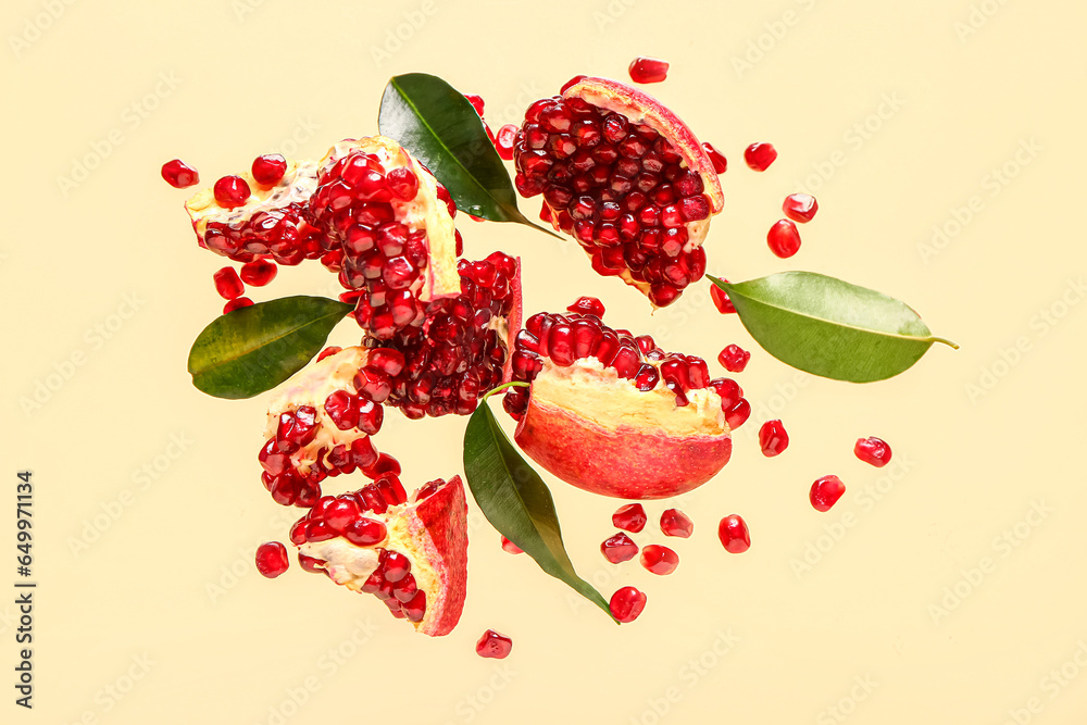 Flying fresh pomegranates with seeds and leaves on yellow background