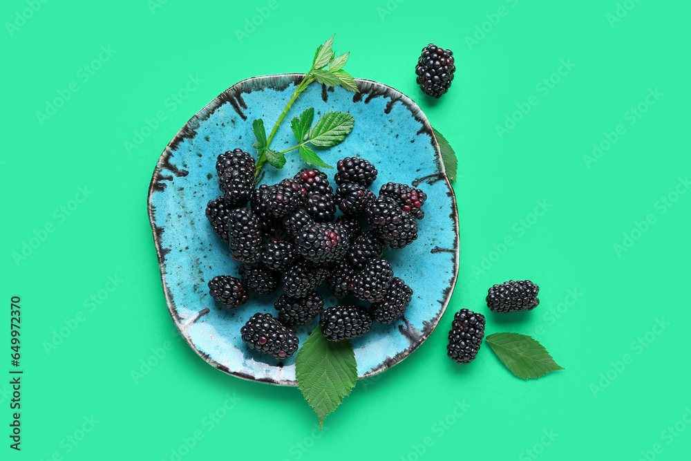 Plate with fresh blackberries and leaves on green background