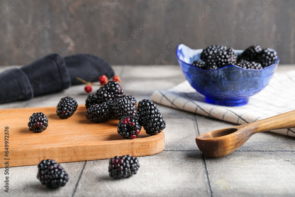 Wooden board and bowl with fresh blackberries on grey tile table