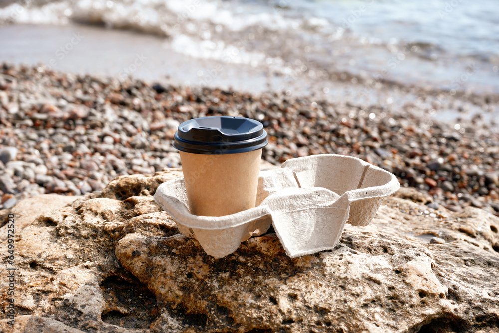 Holder with takeaway cup of hot coffee on beach