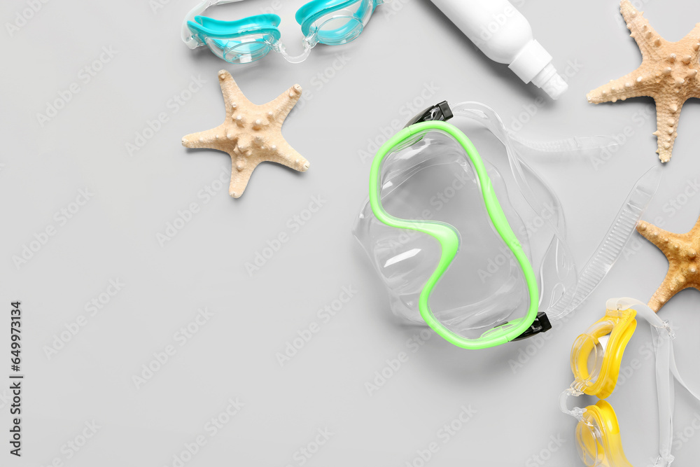 Composition with snorkeling mask, googles, cosmetic product and starfishes on grey background