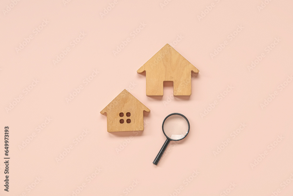 Wooden house figures with magnifier on pink background. Concept of buying real estate