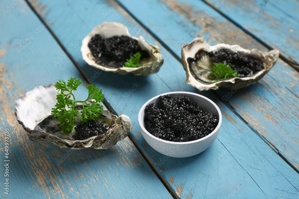 Tasty oysters with black caviar on blue wooden background