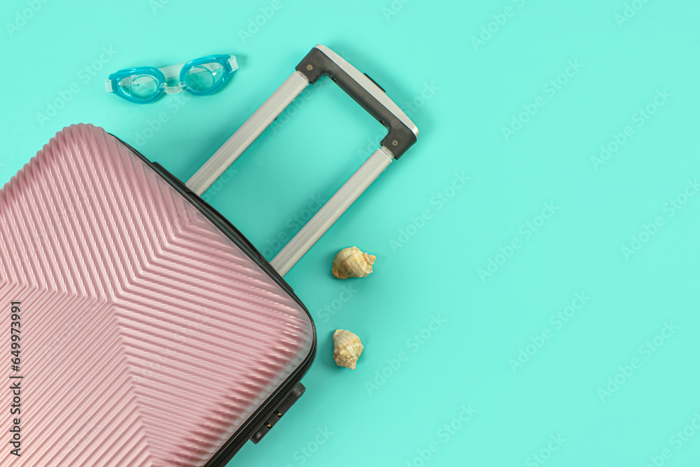 Stylish suitcase, goggles and seashells on color background