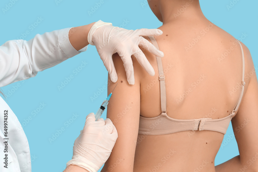 Dermatologist taking puncture from young womans mole on blue background, closeup