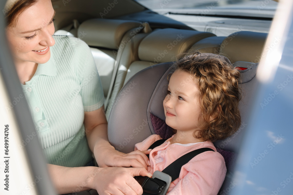 Mother fastening her daughter in child safety seat inside car