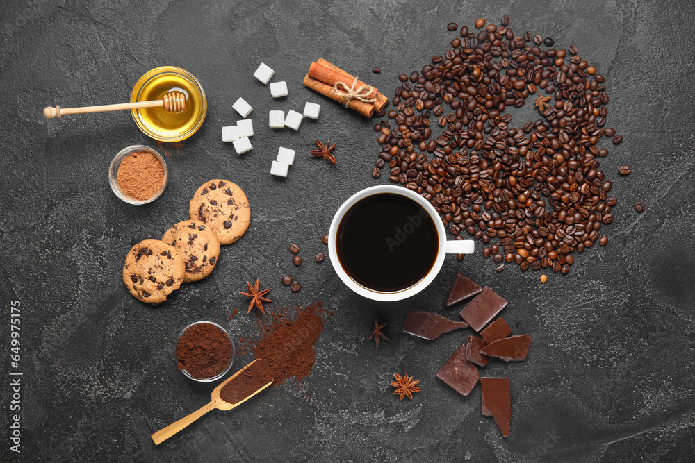 Cup of tasty coffee with cinnamon, beans, chocolate, honey, sugar and cookies on black background