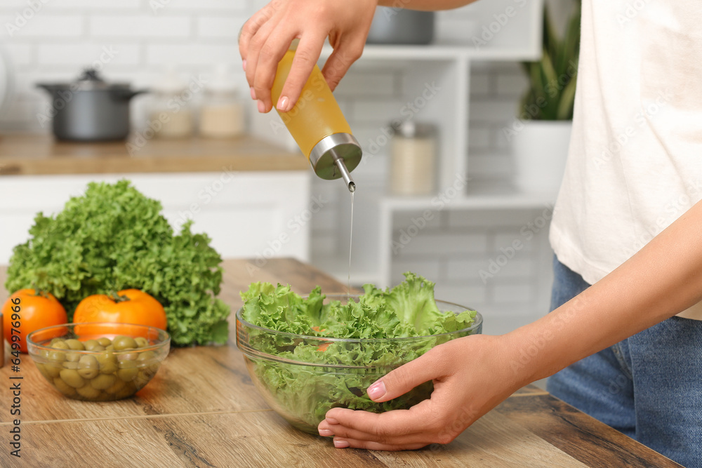 Woman adding olive oil into bowl with tasty salad at table in kitchen