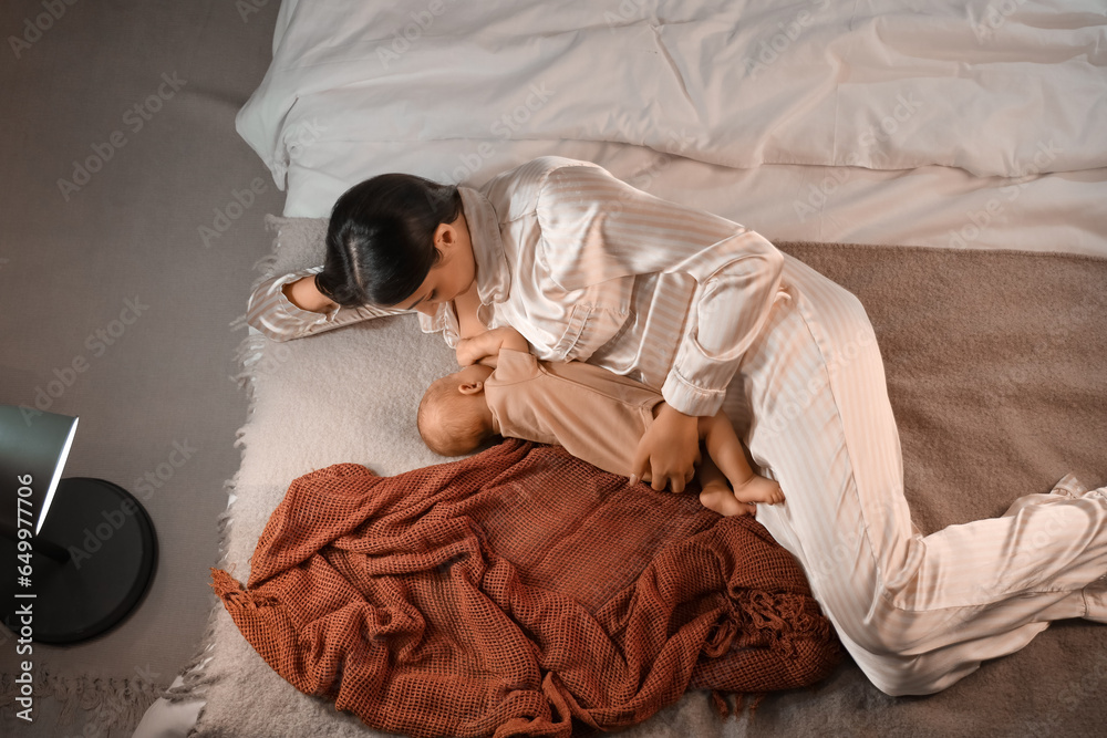 Young woman breastfeeding her baby in bedroom at night, top view