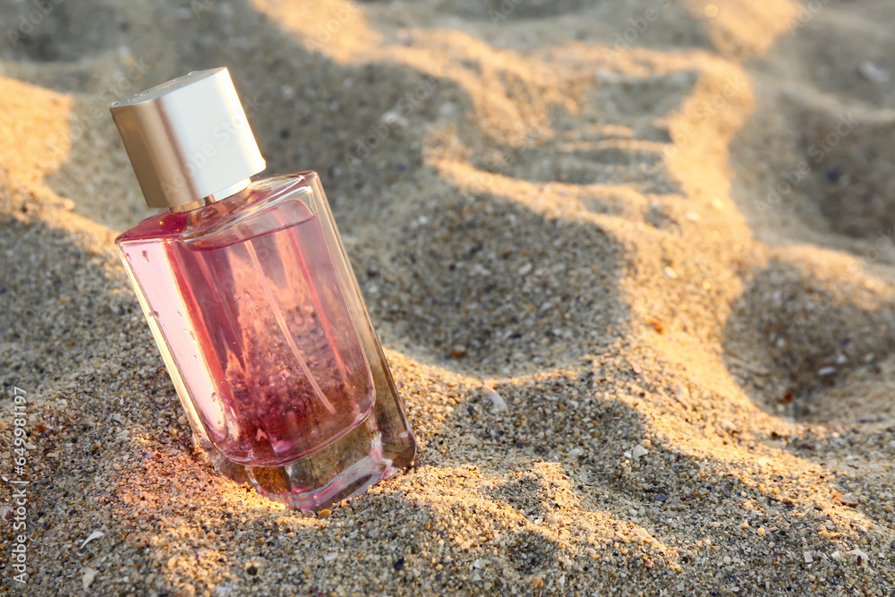 Pink perfume bottle on beach sand, closeup