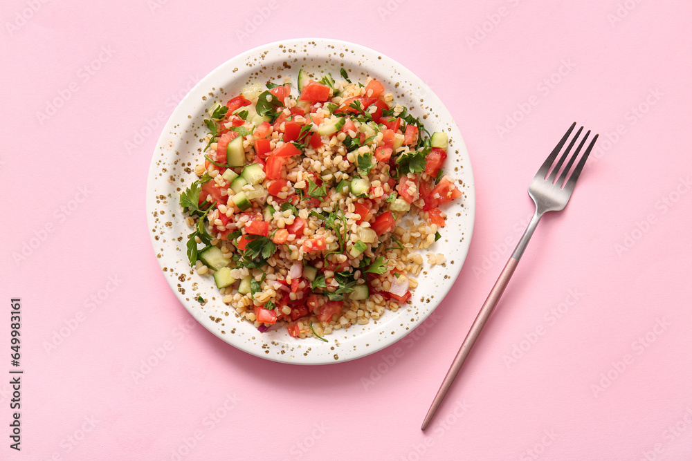 Plate with delicious tabbouleh salad and fork on pink background