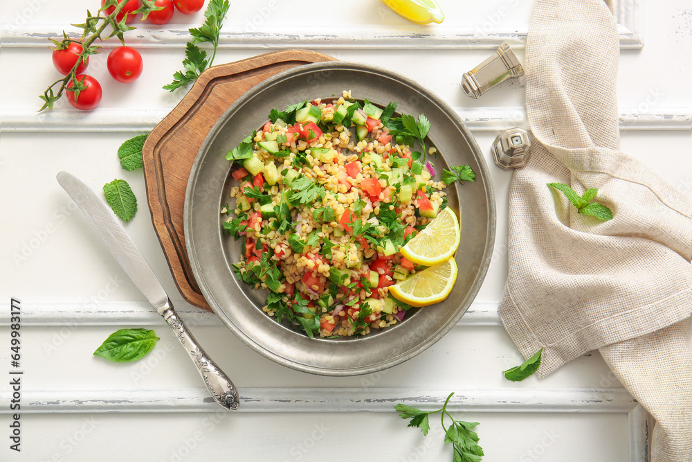 Plate with delicious tabbouleh salad on light wooden background