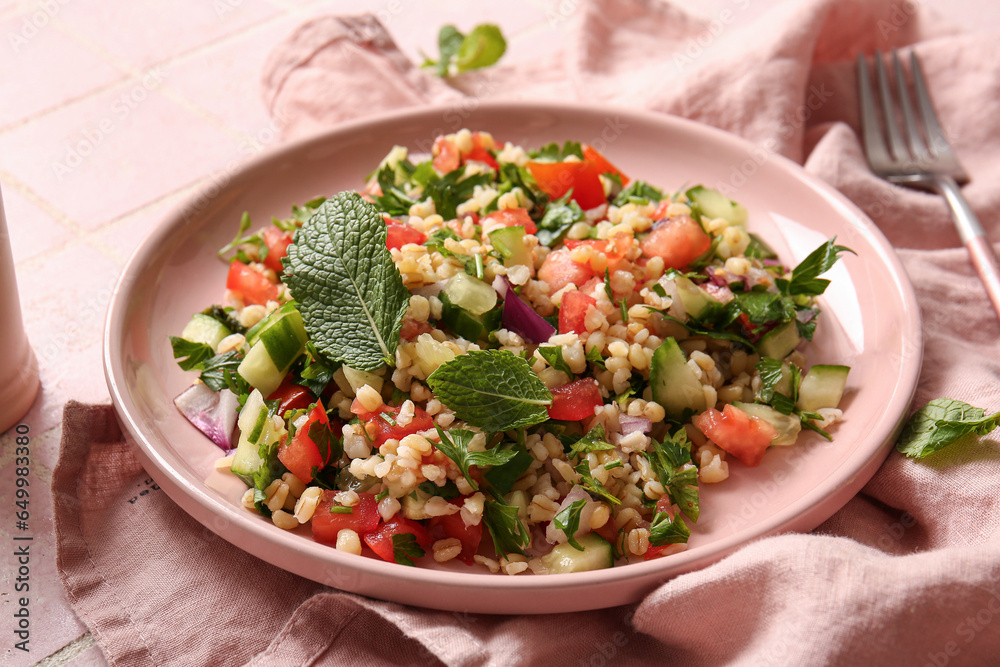 Plate with delicious tabbouleh salad on pink tile background, closeup