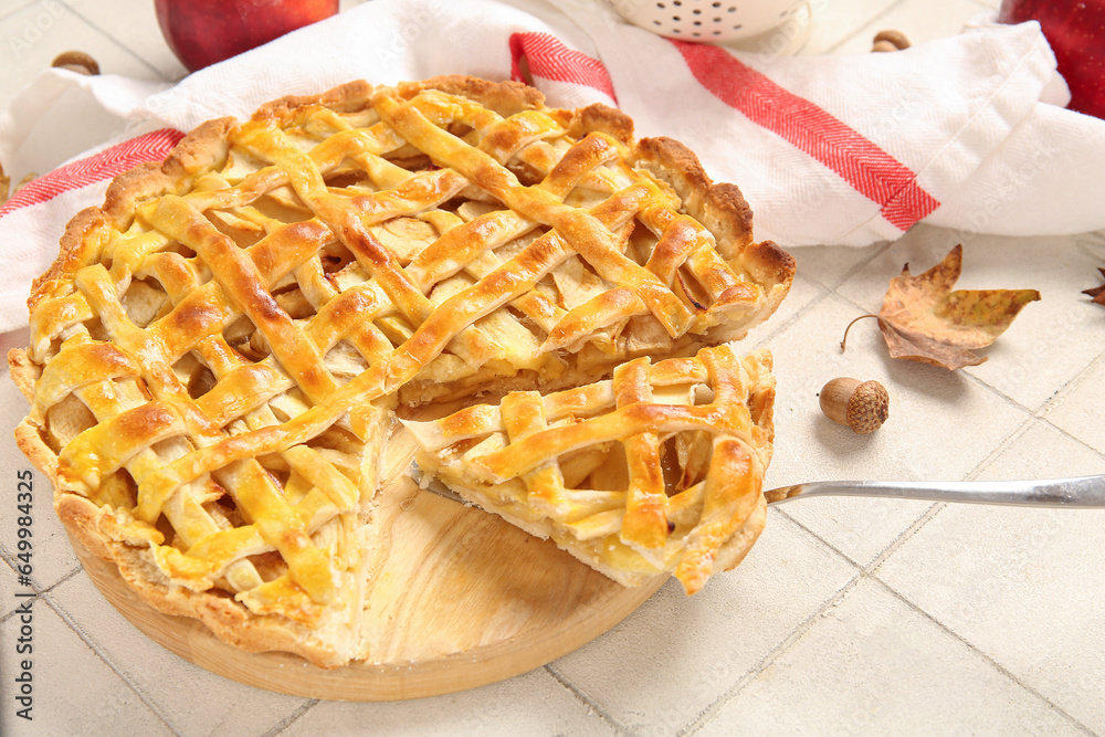 Wooden board with delicious apple pie on white tile background