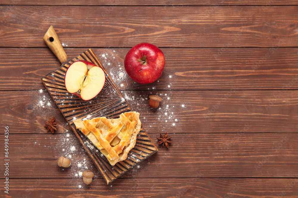 Board with piece of delicious apple pie and ingredients on wooden background