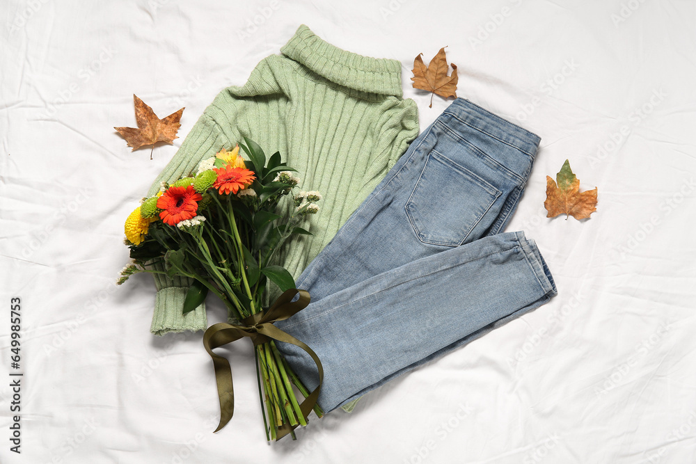 Beautiful autumn composition with stylish clothes, leaves and bouquet of flowers on white bed sheet