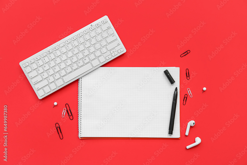 Composition with blank notebook, stationery, keyboard and earphones on red background