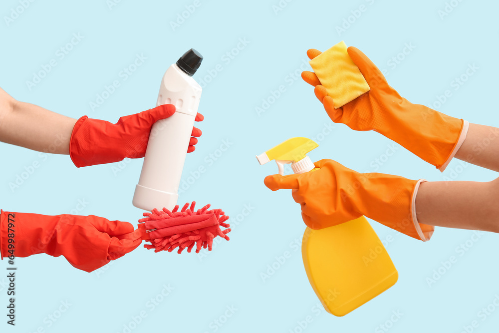 Female hands in rubber gloves holding cleaning products on blue background