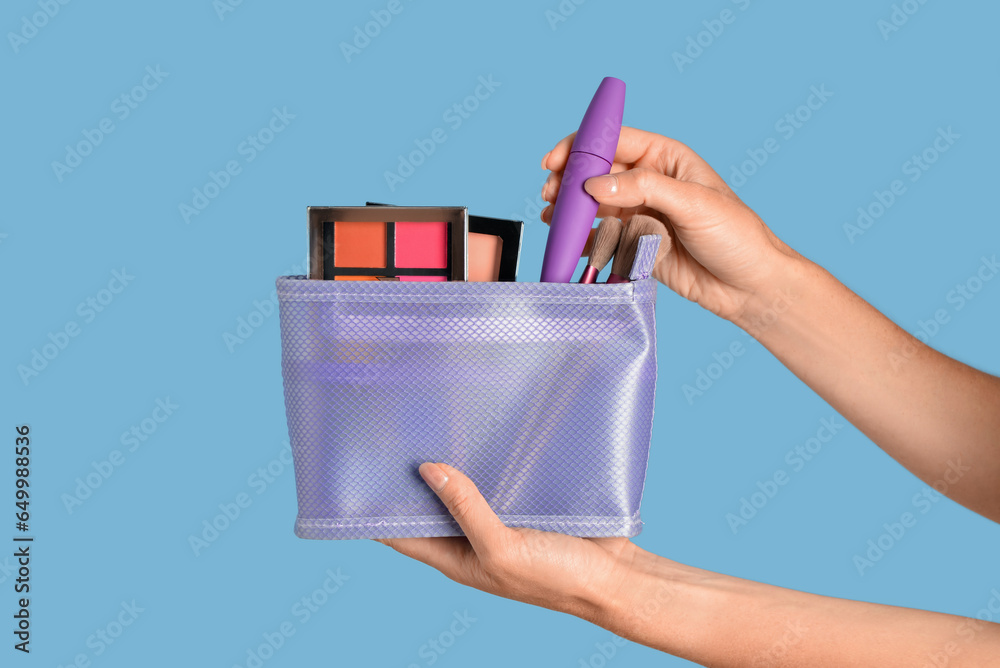 Woman holding bag with decorative cosmetics on blue background