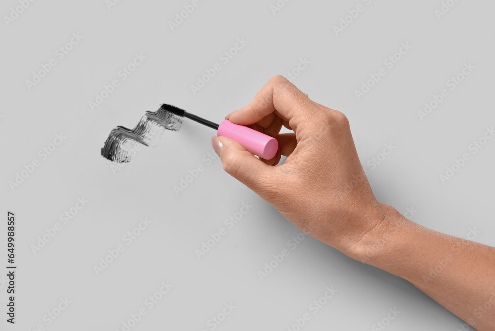 Woman holding black mascara brush and sample on white background